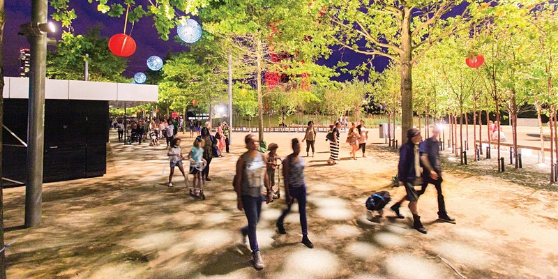 People walking among trees and lanterns in a pedestrianised public space