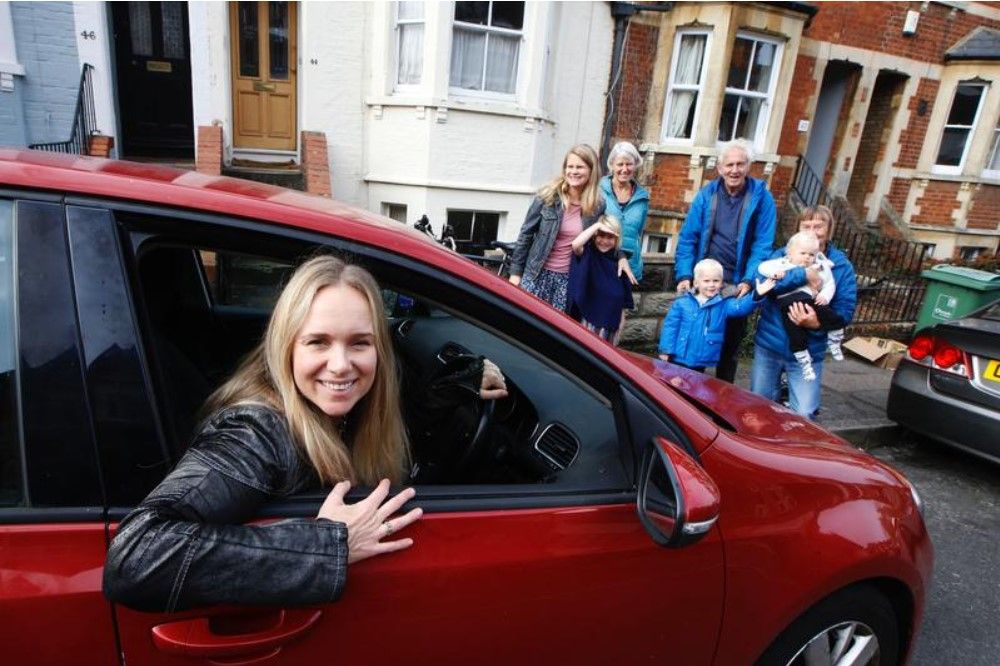 Emily Kerr of shareourcars behind the wheel of a red car with a group of people in the background