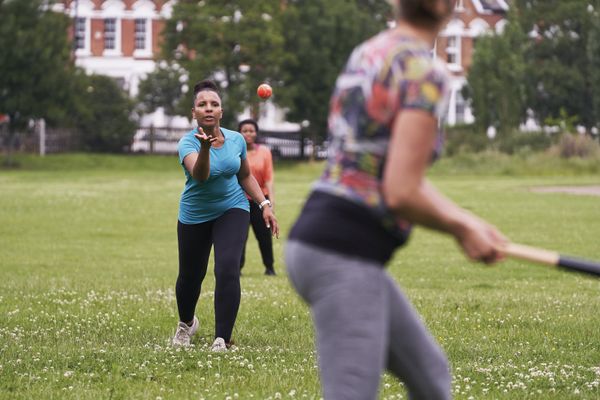 A game of rounders in a park: one woman bowls and another bats