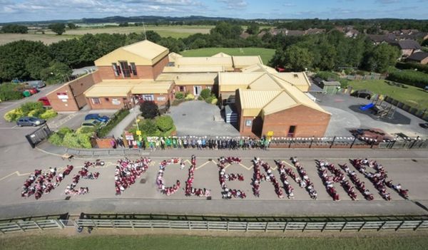 Aerial view of children spelling out “We (heart) clean air” in front of school buildings