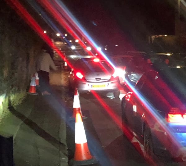 On a congested, dark, narrow road, a motorist moves cones placed alongside a narrow pavement